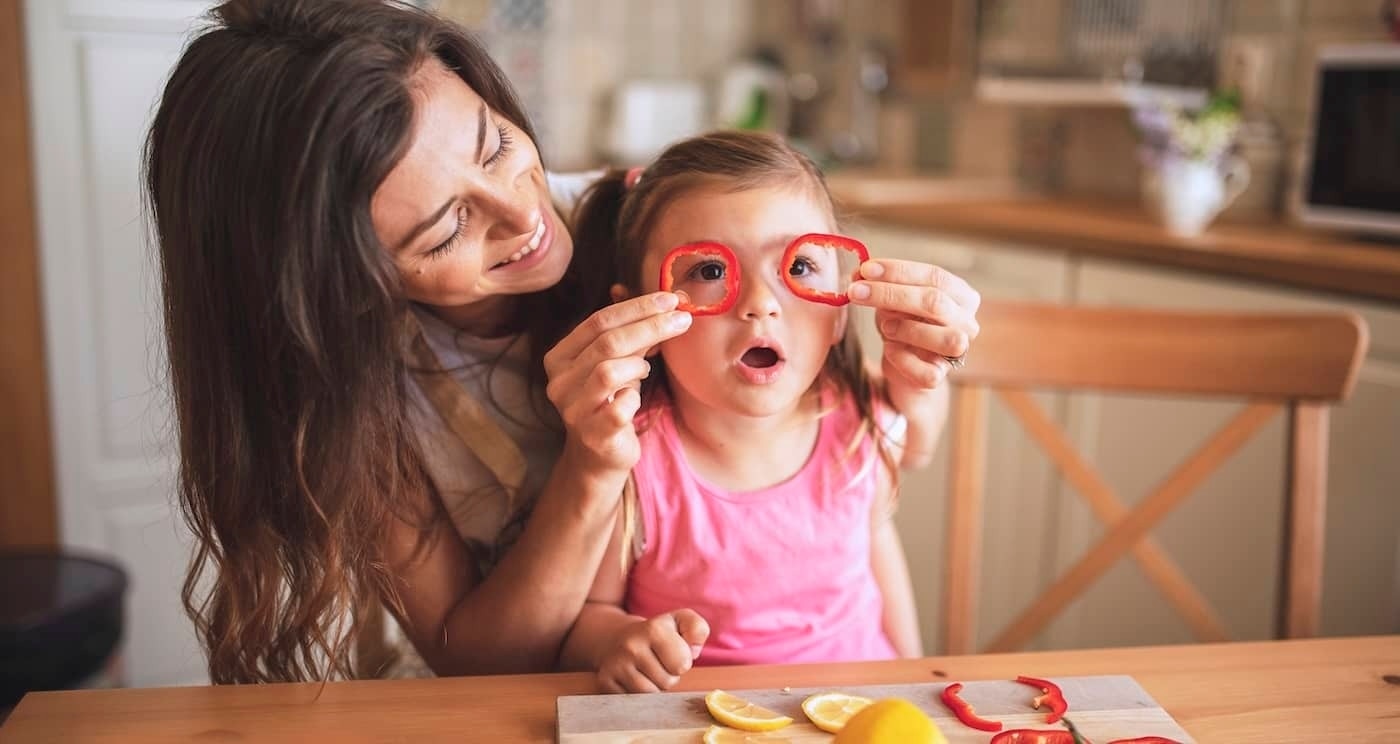 Mère et fille dans la cuisine en train de couper des légumes et de jouer ensemble.